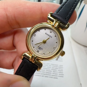 Close-up of women's quartz watch featuring a gold case, crystal dial, and black leather strap