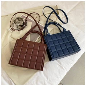 Detail view of square quilted crossbody bags in brown and dark blue on a fabric surface