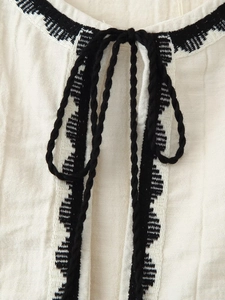 Detail of bohemian ivory cotton vest with black embroidered patterns and neck ties