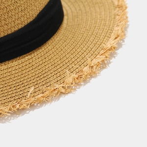 Close-up of woven straw hat with frayed edge detail and black ribbon decoration