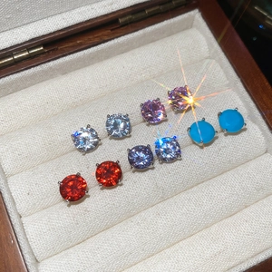 Macro shot of six pairs of round-cut zircon studs in various colors inside a wooden jewelry box