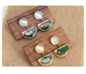 Detail of gold and silver earrings with white cat eye stones and green resin textures