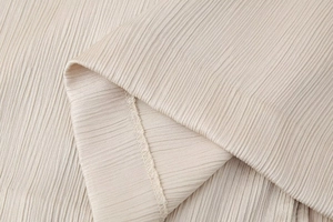 Detalle macro de tela plisada beige con finos pliegues verticales y costuras