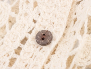 Dettaglio di un bottone rustico in legno su un cardigan beige in maglia crochet traforata