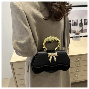 Detail of black bow handbag featuring a wavy edge and bold gold-tone metal handle