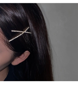 Close-up of a sparkling gold X-shaped rhinestone hair clip worn on dark hair