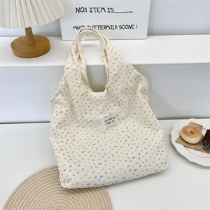 Détail du sac cabas en velours côtelé à fleurs avec écusson sur un support blanc