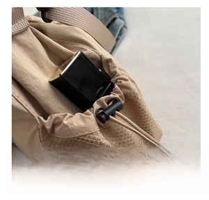Detail of beige nylon drawstring bucket bag with mesh side pocket and adjustable cord