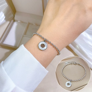 Detail of silver beaded bracelet with mother of pearl coin charm on a model's wrist