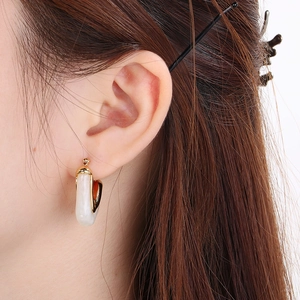 Close-up of model wearing gold V-shaped earrings with white resin inlay details