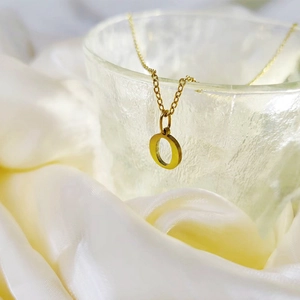 Macro detail of a polished golden letter O pendant on a delicate stainless steel chain