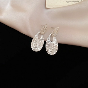 Macro detail of silver oval textured pendant earrings on silk and velvet background