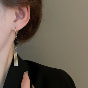 Detail of silver geometric drop earring with black beads worn by a model in suit