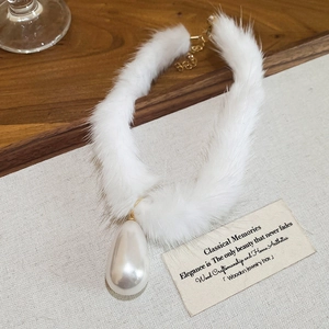 Close-up of white plush fur choker with a large teardrop pearl pendant and gold hardware