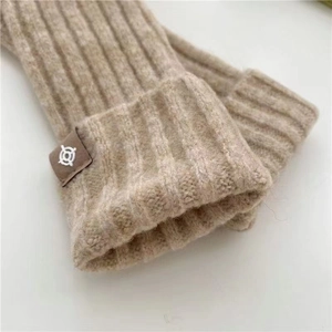 Detail of beige wool knit fingerless gloves featuring a brown leather logo patch on the cuff