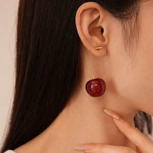 Deep red resin cherry drop earrings with gold metallic finish on a female model
