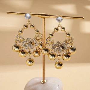 Detail of gold flower earrings with zircon pavé and metallic sphere fringe on a stand