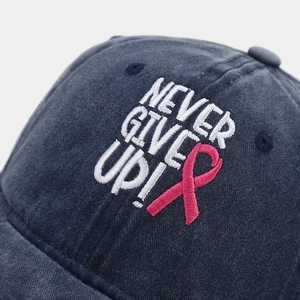 Close-up of pink ribbon and Never Give Up embroidery on washed denim baseball cap