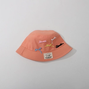 Detail of kids pink bucket hat featuring colorful bows and a white brand label