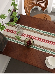 Detail of woven table runner with red and green diamond patterns on a wooden dining table