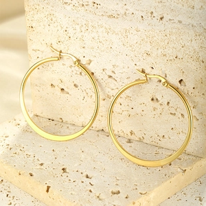 Close-up of thick flat gold hoop earrings displayed on a minimalist beige stone background