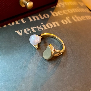 Detailed close-up of adjustable gold pearl ring with a smooth metal bean on vintage book