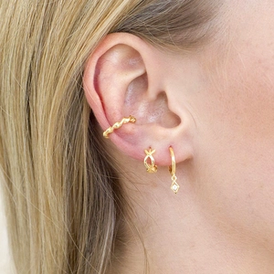 Close-up of triple layered gold earring set with textured cuff and diamond pendant