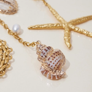 Detail showing the golden conch pendant with a white pearl on a nautical seashell background