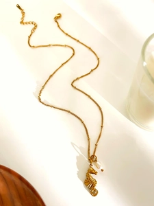 Macro shot of gold seahorse pendant with white pearl on a delicate beaded chain