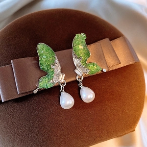 Macro detail of butterfly earrings with green stones and elegant pearl drop charms