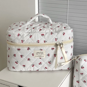 Quilted makeup bag with red cherry prints and beige ribbon handle for travel storage