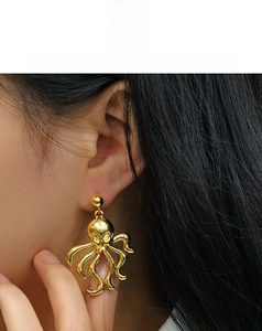Close-up of a gold-colored octopus earring with wavy tentacles worn by a model