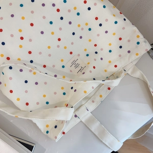 Detail of white canvas tote bag with colorful polka dots and a stitched logo label
