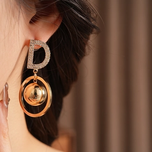 Close-up of golden D-letter earrings with small pavé crystals on a female model