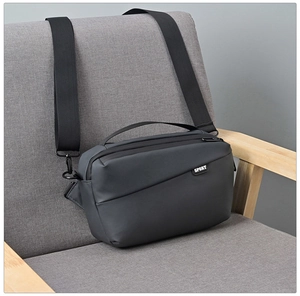 Detail of dark grey commuter crossbody bag on a grey chair with wide black strap