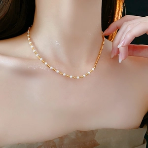 Detail of minimalist asymmetric necklace with gold beads and white pearls on model collarbone