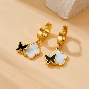 Close-up of gold earrings featuring white shell flower and black butterfly pendants
