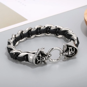 Close-up of woven black leather and silver steel bracelet with dual skull clasp detail