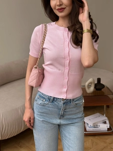 Cardigan in maglia rosa a maniche corte con bottoni e jeans blu in un ambiente domestico
