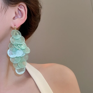 Detail of layered light green shell tassel earrings with translucent disc dangles