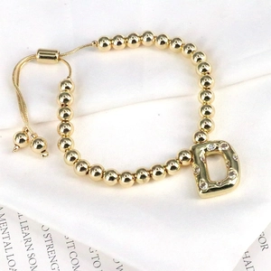 Detail of gold beaded bracelet featuring a sparkling zircon D letter charm and slider clasp