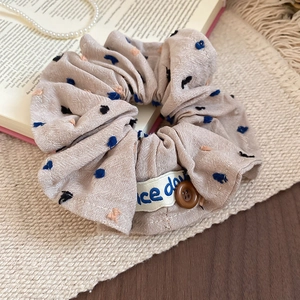Detail of beige pleated fabric scrunchie with colorful embroidery and resin button accent