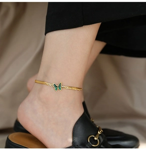 Close-up of gold snake chain anklet with a green butterfly pendant on ankle