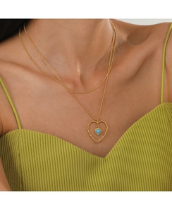 Détail d'un collier doré à deux rangs avec un cœur évidé et pierre bleue sur un mannequin