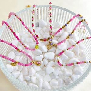 Detail of colorful natural stone beaded necklaces and gold pendants in a glass bowl