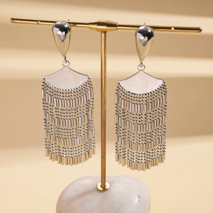 Detailed macro view of silver fan-shaped tassel earrings on a golden display stand
