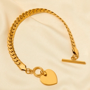 Detail of a gold Cuban link bracelet with heart pendant and OT toggle clasp on beige silk