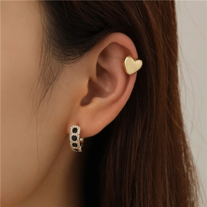 Detailed view of a gold heart ear cuff and black gemstone hoop earring on ear