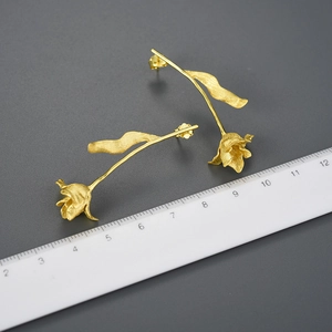 Detail view of gold tulip long earrings with matte brushed finish next to a scale ruler