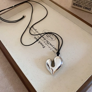 Retro hollow silver heart pendant on black cord resting on vintage book pages